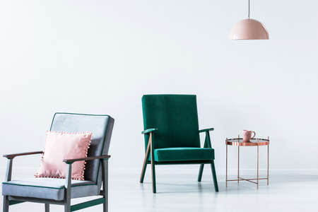 Comfortable, old-fashioned armchairs with wooden frame and pastel pink decorations in a white, empty...