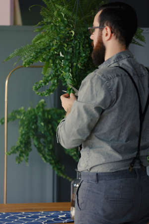 Hipster in grey shirt interested in biology holding a plant at home
