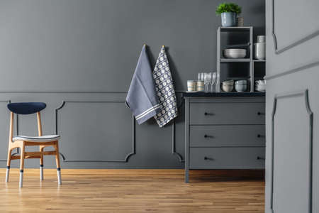 Wooden chair against grey wall with molding and textiles in kitchen interior with cabinet