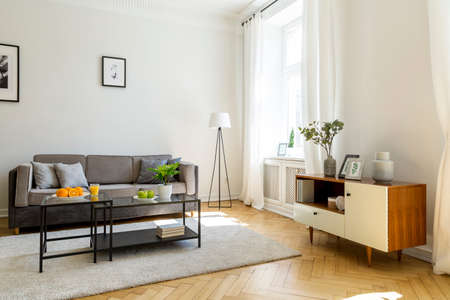 Black table on carpet in front of grey sofa in living room interior with cupboard and poster. Real photoの写真素材