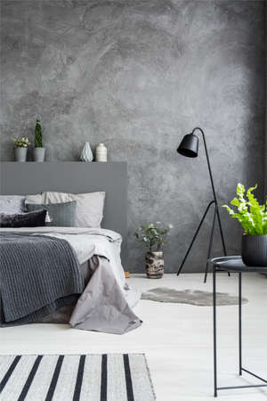 Plant on table in dark monochromatic bedroom interior with lamp next to bed. Real photoの写真素材