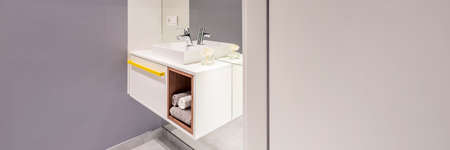 Side view of modern washbasin with a cabinet and towels next to an empty wall in bathroom interior