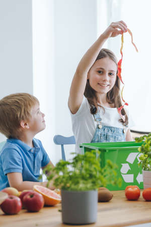 Girl throwing away biological waste into a trashcan while her brother is looking at her