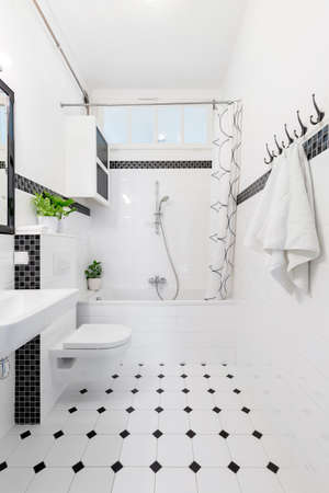 Patterned floor in white and black bathroom interior with towels, toilet and bathtub. Real photo