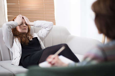Depressed woman holding her head while sitting on a couch in a psychiatrist officeの写真素材