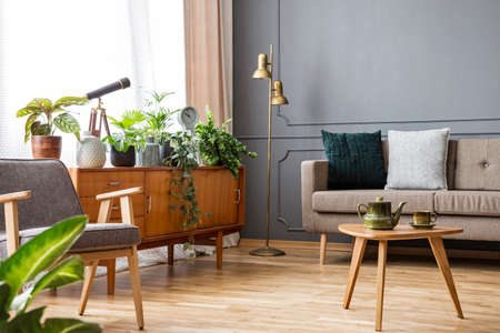 Wooden table in vintage living room interior with cabinet between sofa and armchair. Real photo