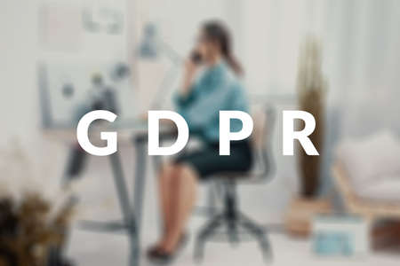 Blurred photo of a businesswoman sitting at her desk, making a phone call behind a GDPR text.の写真素材