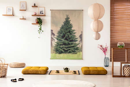 Japanese dining room interior with a tree poster, lamp, pillows and tatami mat with pot and cups on the floorの写真素材