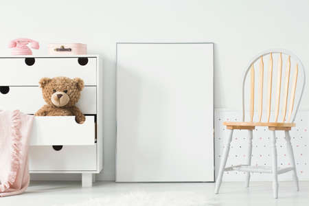 Poster with mockup between chair and cabinet with teddy bear in kid's room interior. Real photo. Paste your poster hereの写真素材