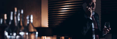 Panorama of a workaholic drinking brandy and talking on the phoneの写真素材