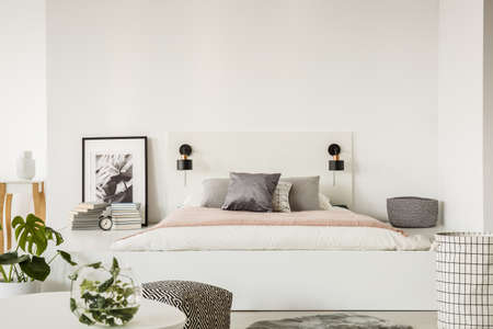 Grey pillow on pink and white sheets of bed on platform in bedroom interior with poster. Real photo