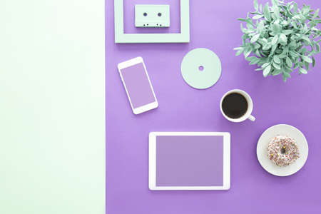 Mockup of freelancer's smartphone and tablet on ultra violet desk with cup of coffee and doughnutの写真素材