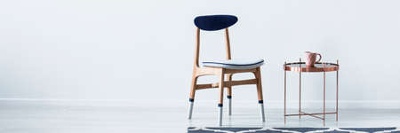 Blue and white wooden chair standing by metal end table with pastel pink mug in bright room interior with place for your cupboardの写真素材