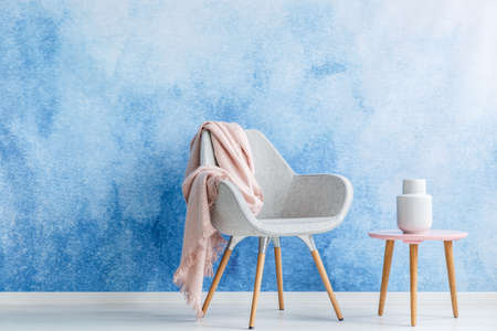 Living room with a blanket on an armchair and coffee table with a white vase set on an ombre wall. Place your productの写真素材