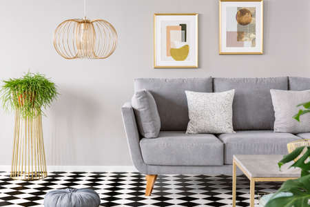 Real photo of a living room interior with gold posters on the walls, grey sofa with cushions and...