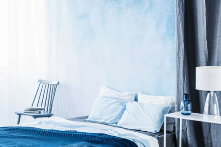 White lamp on table next to bed with navy blue bedding in bedroom interior with ombre wall