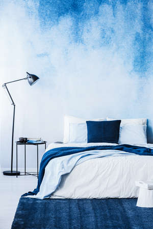 Navy blue carpet in front of bed next to lamp in bedroom interior with wallpaperの写真素材
