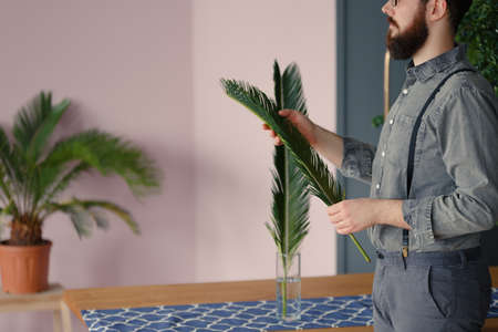 Close-up of man with beard wearing a grey shirt putting palm leaves into a glass vaseの写真素材