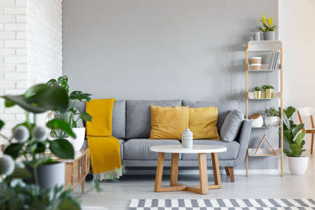 Orange pillows and blanket on grey couch in living room interior with wooden table. Real photoの写真素材