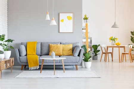 Orange blanket on grey sofa in modern apartment interior with poster and wooden table. Real photoの写真素材