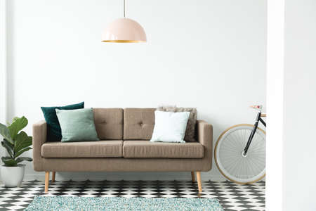 Modern sofa with green pillows under a pink lamp, bike and plant set in a living room interiorの写真素材
