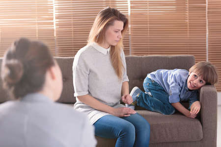Boy with ADHD playing around during a family therapy session next to his sad motherの写真素材