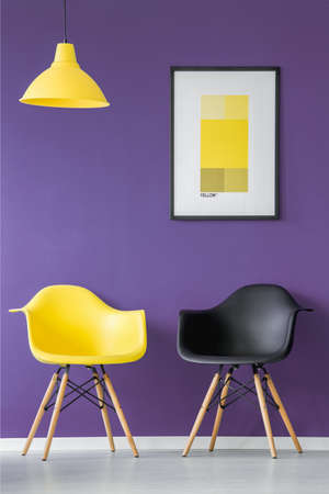 Yellow and black chair, poster and lamp on a purple wall in office interiorの写真素材