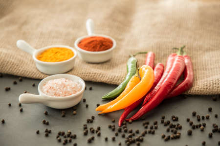 Chili peppers, salt, turmeric powder and red pepper powder on a table with black pepper strewn aroundの写真素材