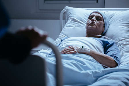 Senior woman with headscarf in hospital bed during chemotherapyの写真素材