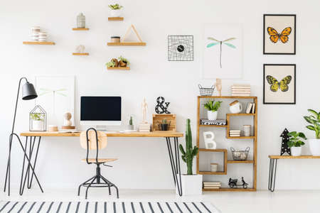 Modern home office interior with a wooden desk, chair, shelves, computer with empty screen and plantsの写真素材