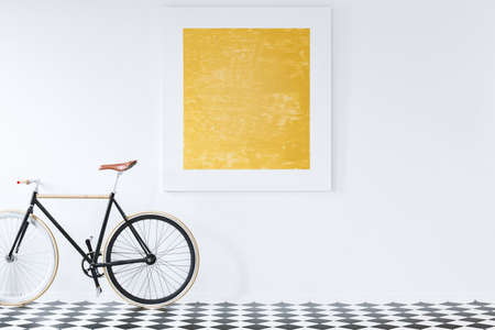 Black bike on checkerboard floor in retro interior with gold painting on white wallの写真素材