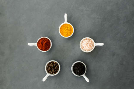 Top view of bowls with spices arranged in a circle on a grey backgroundの写真素材
