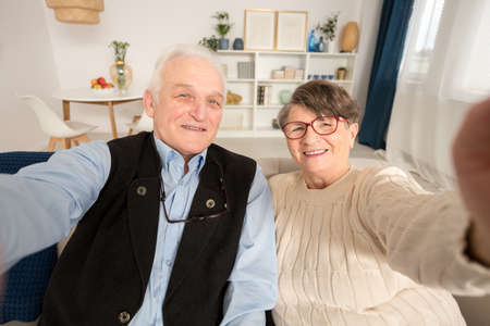 Happy senior marriage taking a selfie in their home in spacious living roomの写真素材