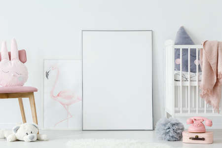 Toys in child's bedroom interior with white bed next to empty poster with mockup. Real photo. Place...