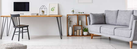 Study corner with black chair and hairpin table with empty monitor, simple poster and cactus in...