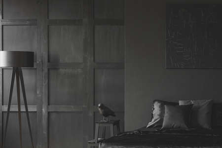 Sculpture on table next to bed against the wall with black poster in minimal bedroom interior with lampの写真素材