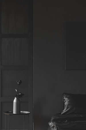 Black rose on table in dark bedroom interior with wooden wall and poster above bed