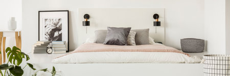 Small lamps placed on white bedhead by the simple mattress bed with pillows in bedroom interior with...