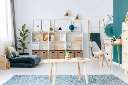 Minimal modern art posters placed on white wooden rack in bright living room interior with desk, folded mattress and fresh plantsの写真素材