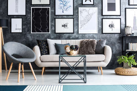 Balls on table in front of beige sofa in grey living room interior with armchair and postersの写真素材