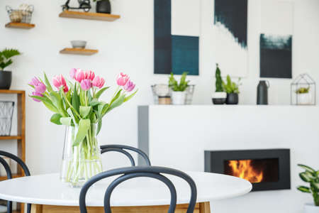 Pink tulips on dining table in white room interior with plants and posters above fireplace. Real photoの写真素材