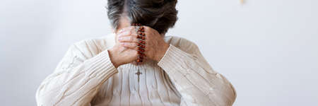 Panorama of catholic grandmother praying with rosary in the churchの写真素材