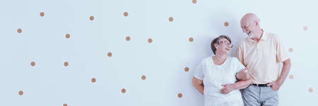 Happy, elderly couple in love looking at each other while posing on a white wall with polka dot pattern and copy space.の写真素材