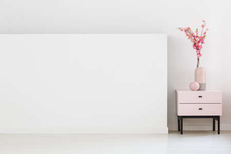 Pink flowers on cabinet next to white wall with copy space in living room interior. Real photo....