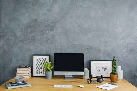 Plants, posters and desktop computer on desk in grey home office interior with copy space. Real photoの写真素材