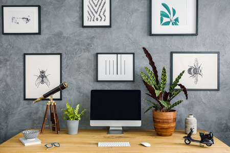 Plants, telescope and desktop computer on wooden desk in work area interior with posters. Real photoの写真素材