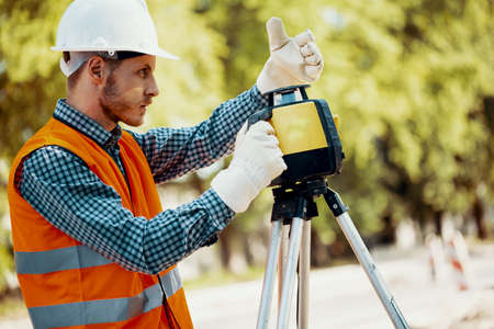 Engineer in uniform and white helmet using professional equipment during roadworks