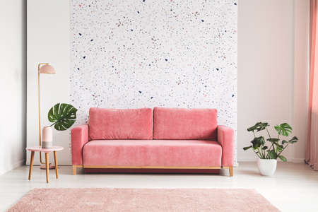 Pink couch between plant and lamp in bright living room interior with patterned wall. Real photoの写真素材
