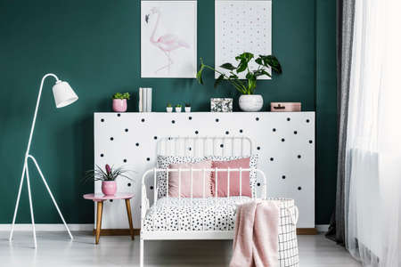 Feminine bedroom interior with a bed, bedside table, lamp, plants and flamingo posterの写真素材