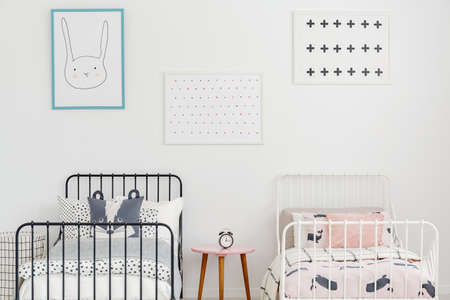 Close-up of two metal frame beds with bedding and posters on a white wall in a room of a private...
